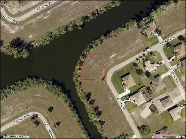This is an aerial map showing a vacant residential lot outlined in red along a canal — 2113 NE 43RD LANE, CAPE CORAL, FL