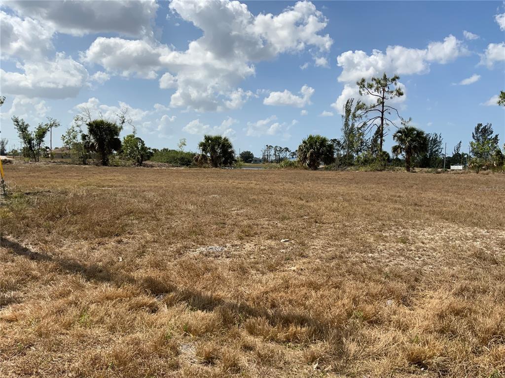 A large, flat, grassy vacant lot under a blue sky with scattered clouds — 2113 NE 43RD LANE, CAPE CORAL, FL