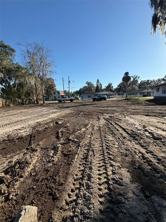 A muddy, unpaved lot with tire tracks leads toward houses and trees under a clear sky — 748 CR 477A, LAKE PANASOFFKEE, FL