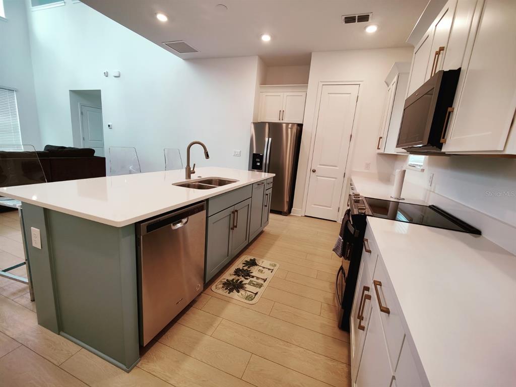 A modern kitchen features a large island, stainless steel appliances, and white cabinetry — 7703 NEMOURS PARKWAY, ORLANDO, FL