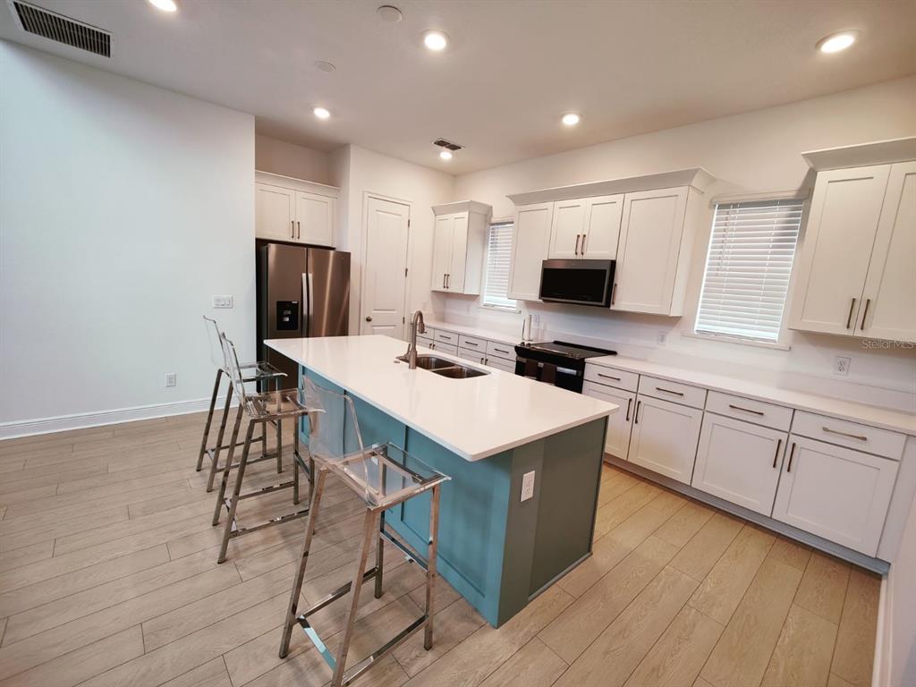 A modern kitchen features white cabinetry, a teal island with bar stools, and light flooring — 7703 NEMOURS PARKWAY, ORLANDO, FL
