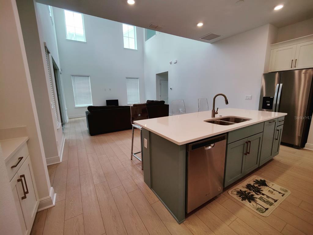A kitchen with a teal island and stainless steel appliances overlooks a two-story living room — 7703 NEMOURS PARKWAY, ORLANDO, FL