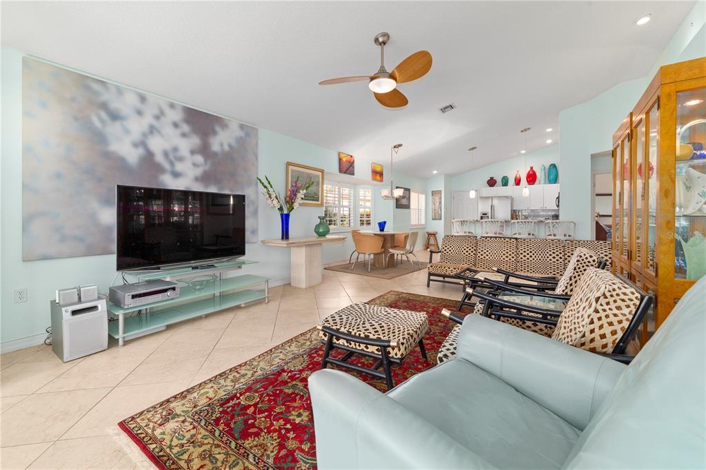 A living room features a large television, patterned furniture, a red rug, and tile floors — 1378 CAPRI ISLES BOULEVARD UNIT 61, VENICE, FL
