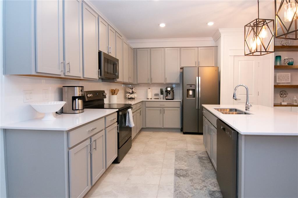 A modern kitchen features gray cabinets, white countertops, stainless steel appliances, and a central island — 2006 MYRTLE PINE STREET, KISSIMMEE, FL