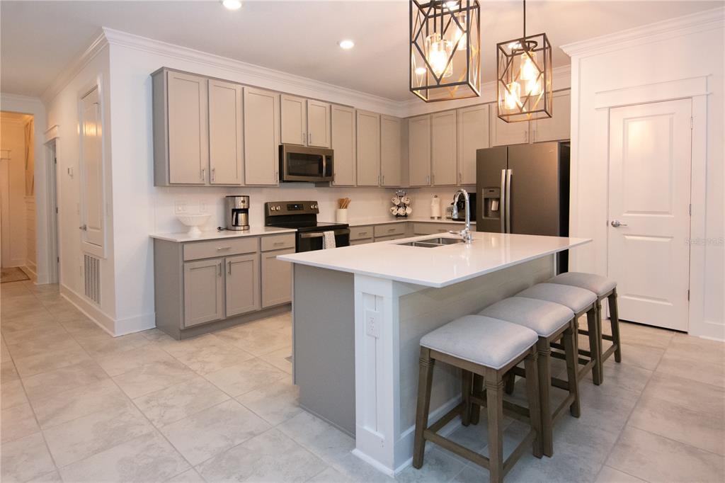 A modern kitchen features gray cabinets, a white quartz island with bar seating, and stainless appliances — 2006 MYRTLE PINE STREET, KISSIMMEE, FL