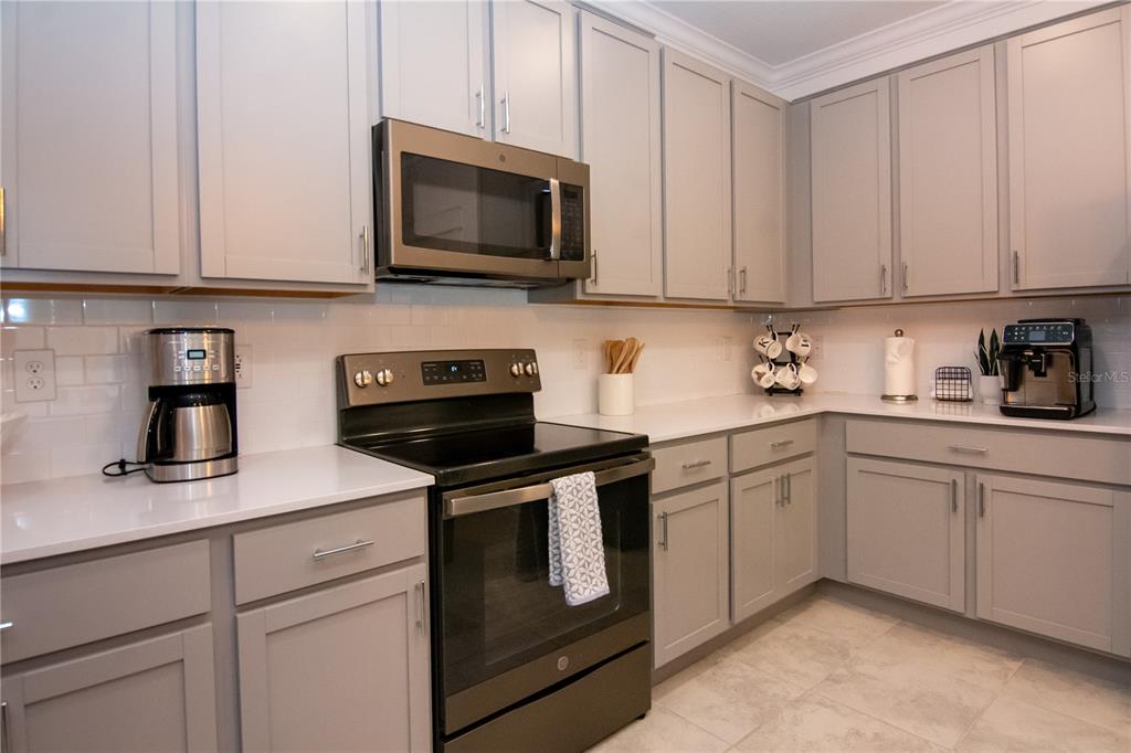 A kitchen features gray cabinets, white countertops, a subway tile backsplash, and stainless steel appliances — 2006 MYRTLE PINE STREET, KISSIMMEE, FL