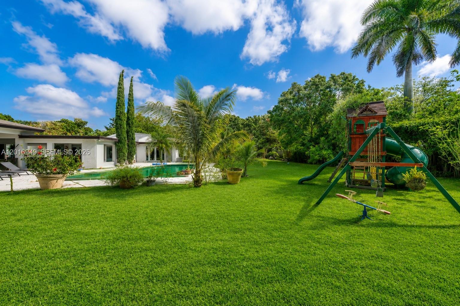 A swimming pool sits in front of a house with a large paved patio — 7650 SW 128th St, Pinecrest FL 33156, PINECREST, FL