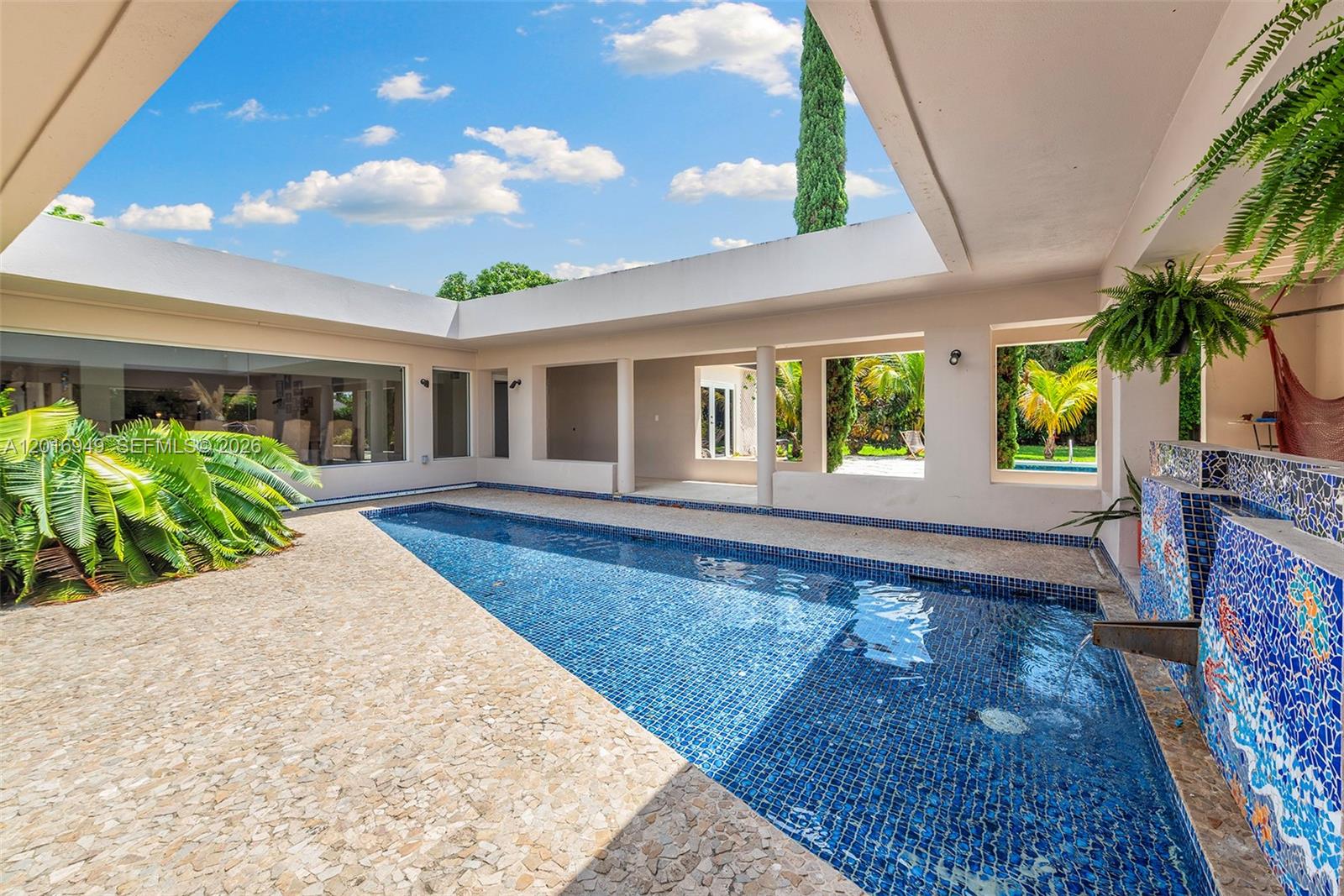 A bright living room features light tile floors, a patterned area rug, and a black door — 7650 SW 128th St, Pinecrest FL 33156, PINECREST, FL