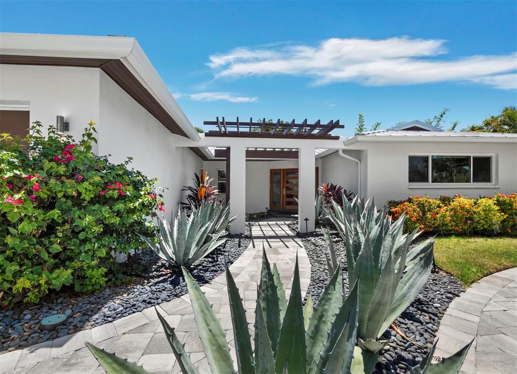 A paved walkway leads to a front entrance framed by a wooden pergola and landscaping — 622 TROPICAL CIRCLE, SARASOTA, FL