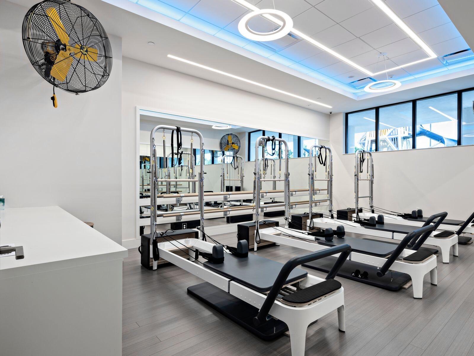 A bright Pilates studio features several reformers, a large wall mirror, and a ceiling fan — 7370 Orangewood Lane # 303, Boca Raton FL 33433, BOCA RATON, FL