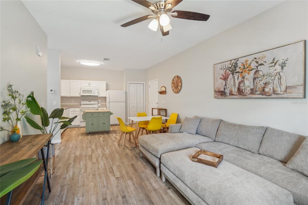 A living room and kitchen area features light wood flooring, a gray sectional, and yellow chairs — 14524 N NEBRASKA AVENUE UNIT 204A, TAMPA, FL