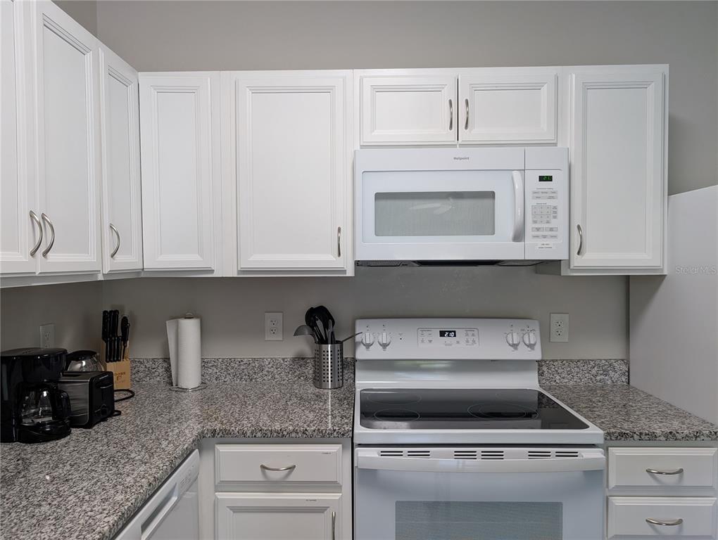 A kitchen features white cabinets, granite countertops, and white appliances including a microwave and stove — 14524 N NEBRASKA AVENUE UNIT 204A, TAMPA, FL