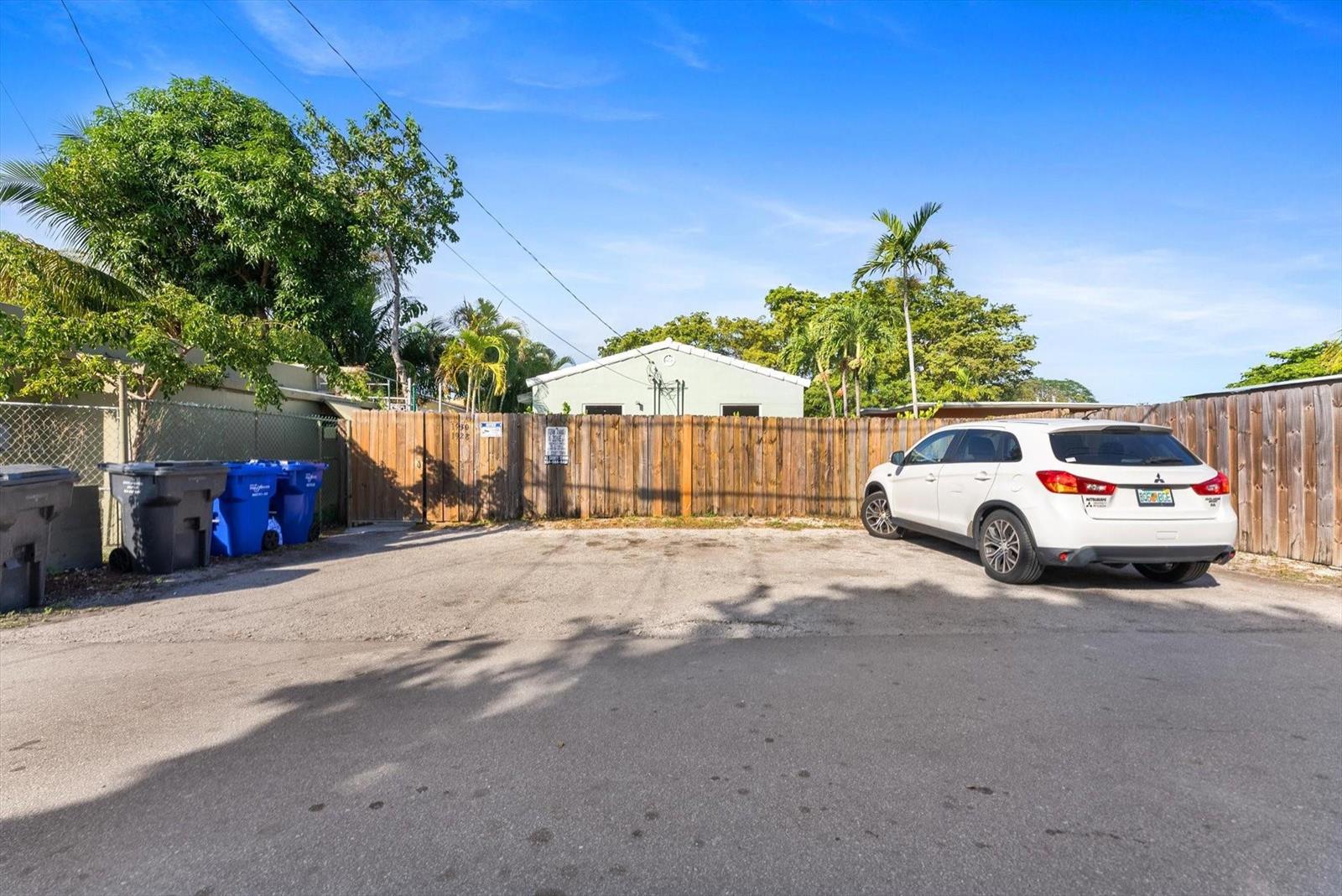 A white SUV is parked in a gravel lot in front of a wooden fence — 1928 Adams Street, Hollywood FL 33020, HOLLYWOOD, FL