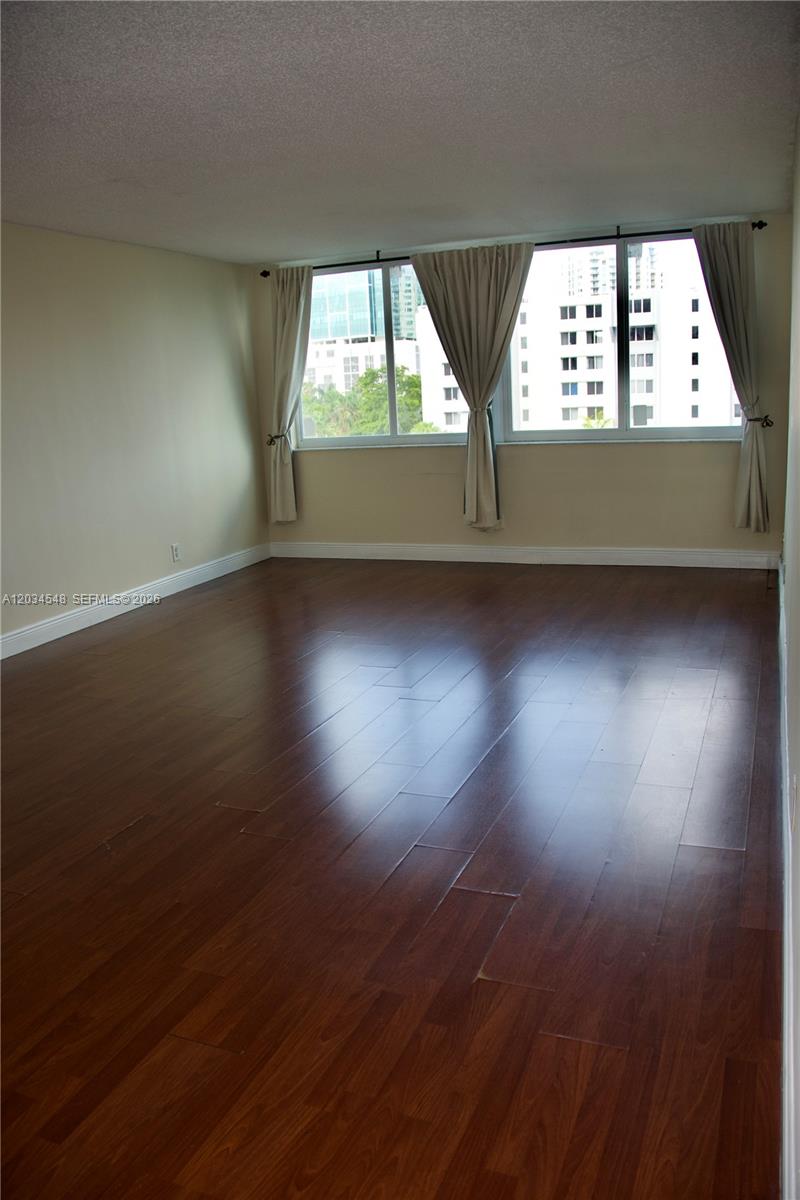 An empty room features dark wood flooring, beige walls, and large windows with beige curtains — 9125 SW 77th Ave # 501, Miami FL 33156, MIAMI, FL