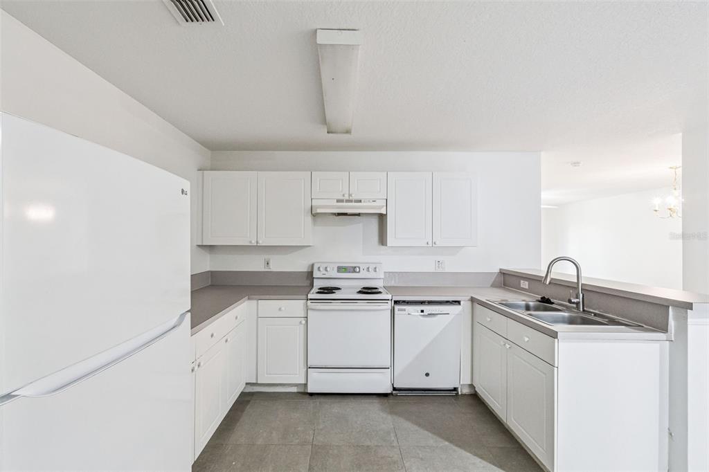 A kitchen with white cabinets, white appliances, gray countertops, and gray tile flooring — 8818 GRAND PALMS CIRCLE UNIT A, KISSIMMEE, FL