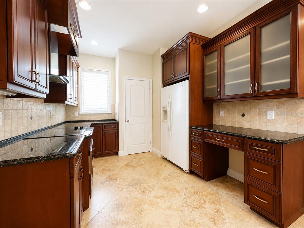A kitchen with dark wood cabinets, granite countertops, tile flooring, and a white refrigerator — 1409 MICHIGAN AVENUE, WINTER PARK, FL