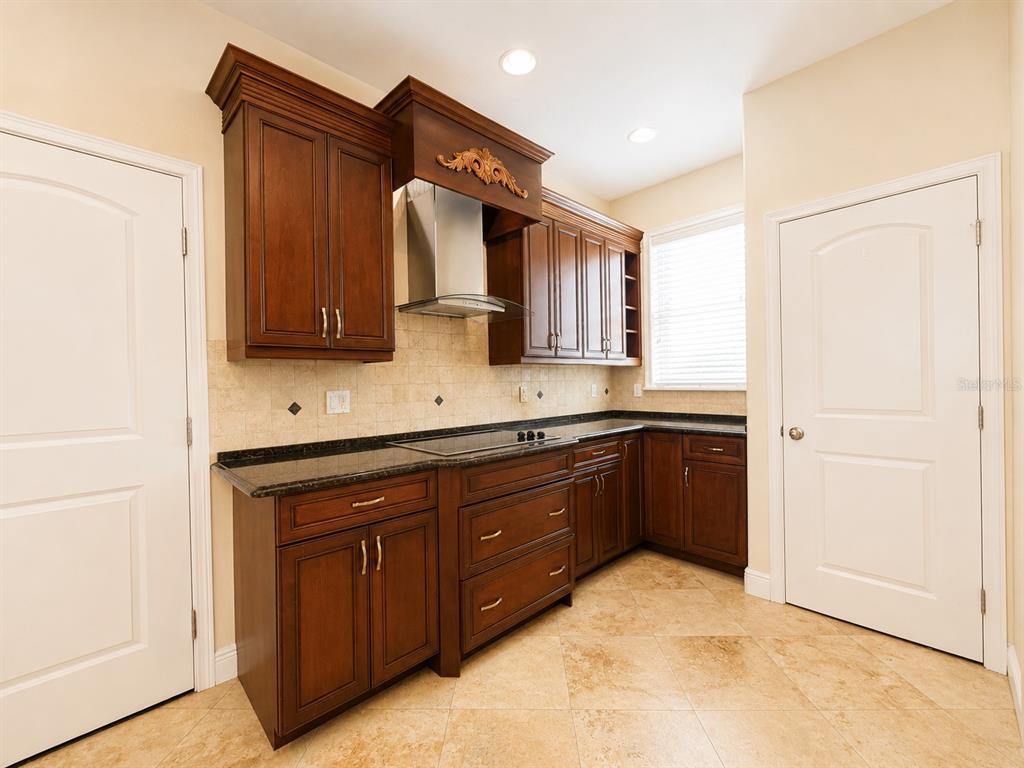 A kitchen features dark wood cabinets, granite countertops, a stainless steel range hood, and tile flooring — 1409 MICHIGAN AVENUE, WINTER PARK, FL