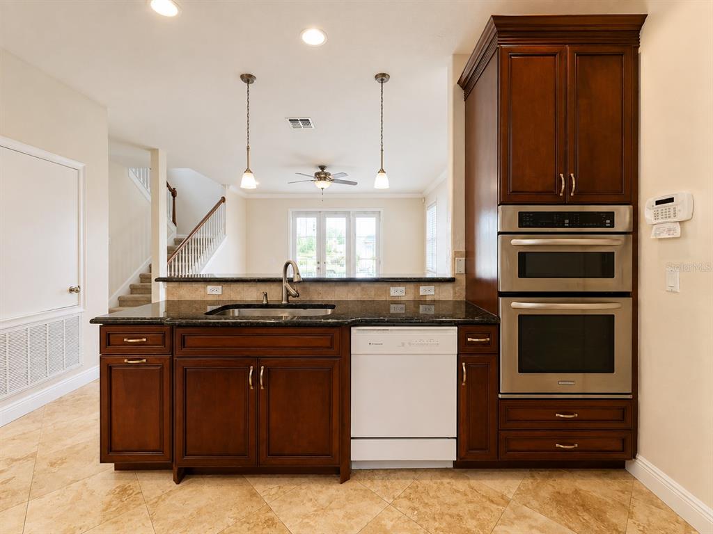 A kitchen features dark wood cabinets, granite countertops, a white dishwasher, and a double wall oven — 1409 MICHIGAN AVENUE, WINTER PARK, FL