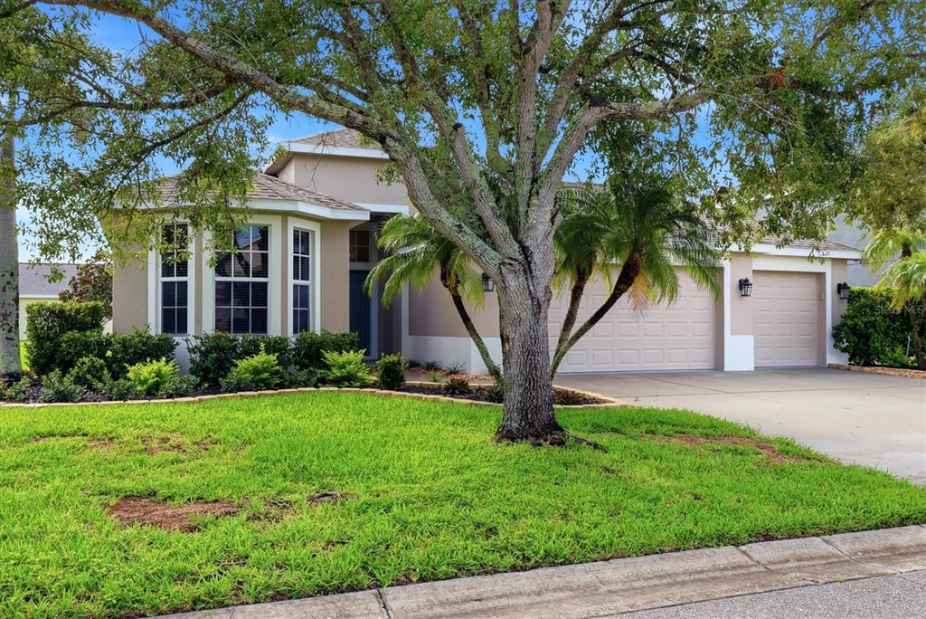 A single-story house with a beige exterior, a three-car garage, and a large front tree — 7117 50TH AVENUE CIRCLE E, PALMETTO, FL