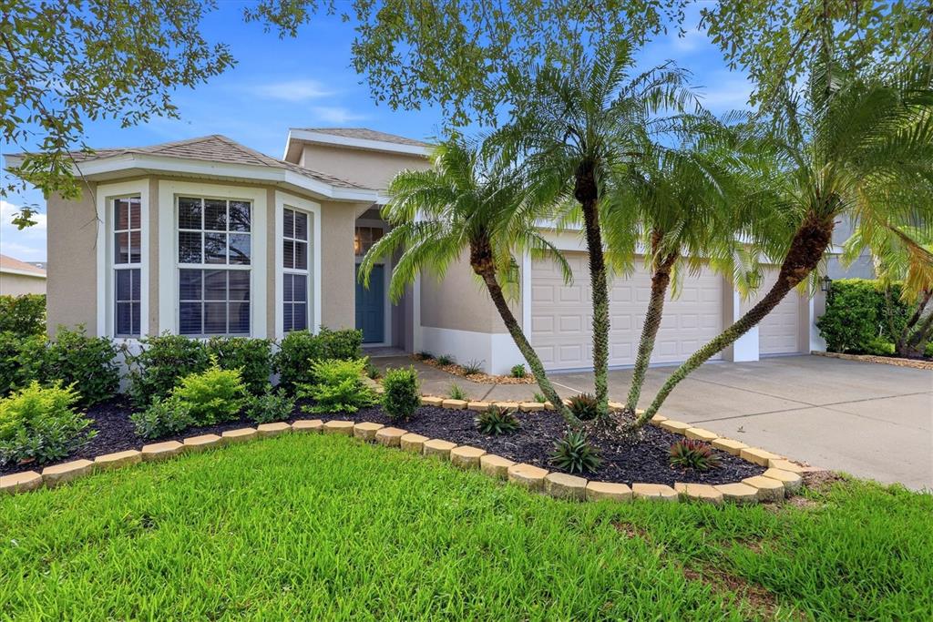 A single-story house with a beige stucco exterior, a three-car garage, and a palm tree — 7117 50TH AVENUE CIRCLE E, PALMETTO, FL