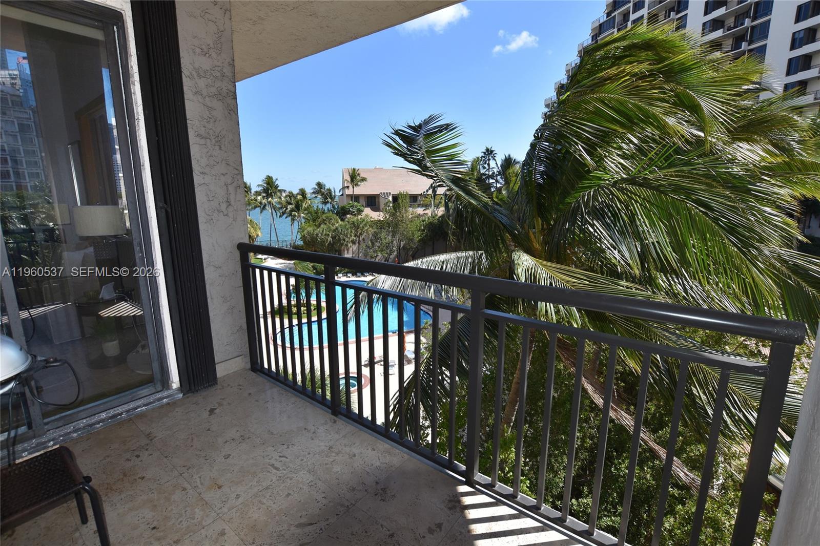 A balcony with stone flooring overlooks a swimming pool, palm trees, and the ocean — 540 Brickell Key Dr # 505, Miami FL 33131, MIAMI, FL