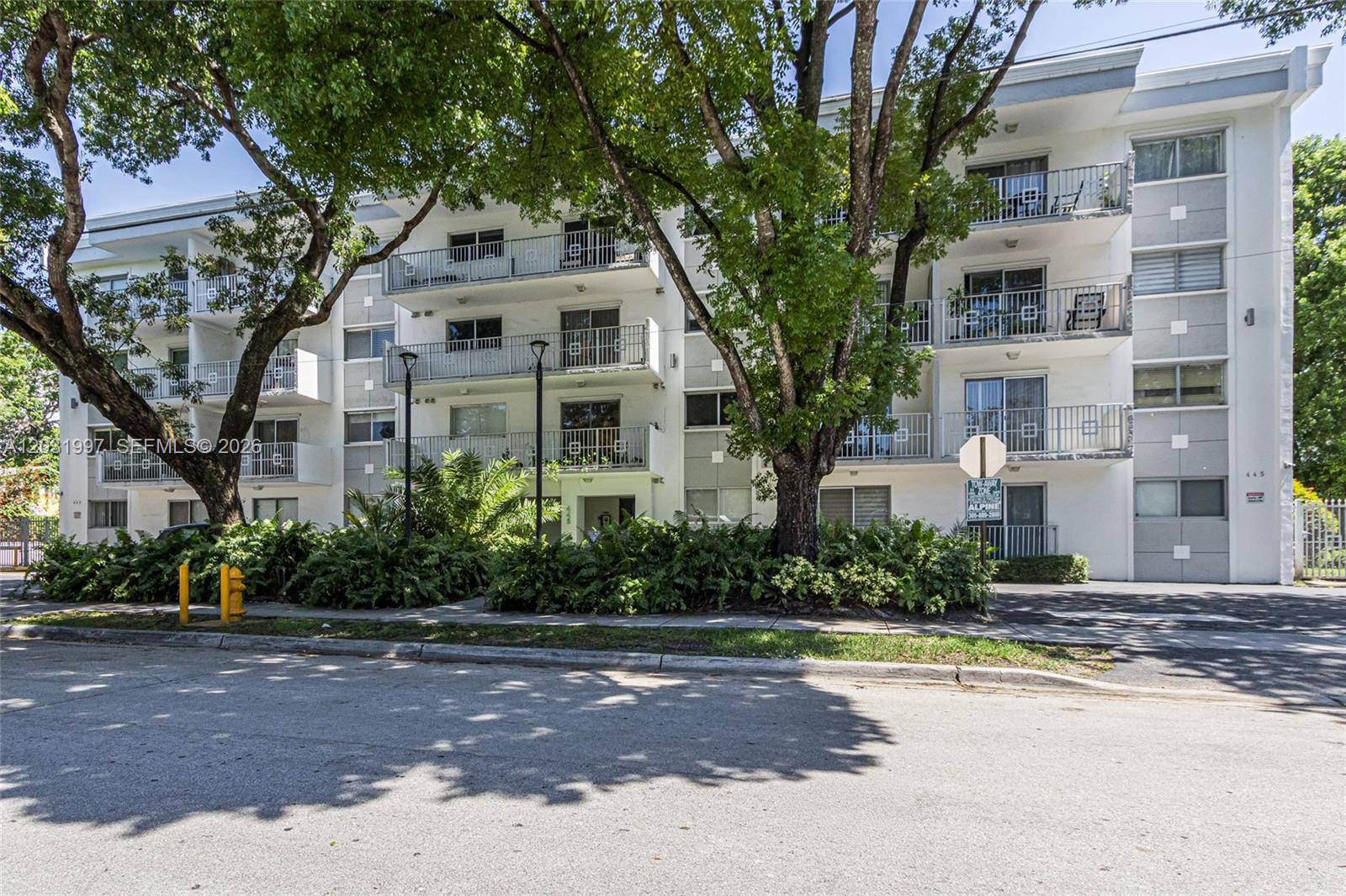 A multi-story white apartment building is surrounded by large trees and lush landscaping — 445 SW 11th St # 102, Miami FL 33130, MIAMI, FL