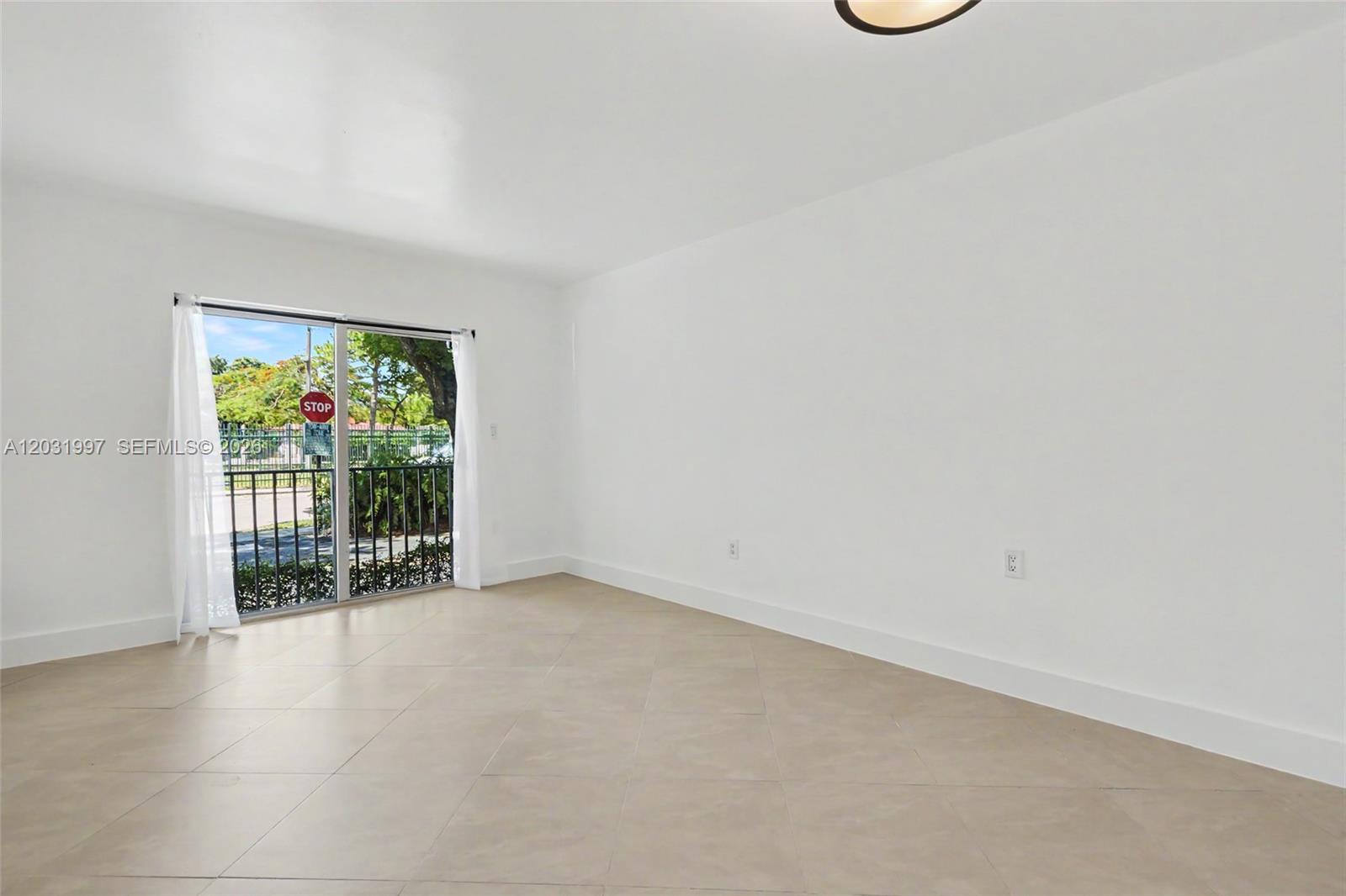 An empty room with white walls, tile flooring, and a sliding glass door to a balcony — 445 SW 11th St # 102, Miami FL 33130, MIAMI, FL