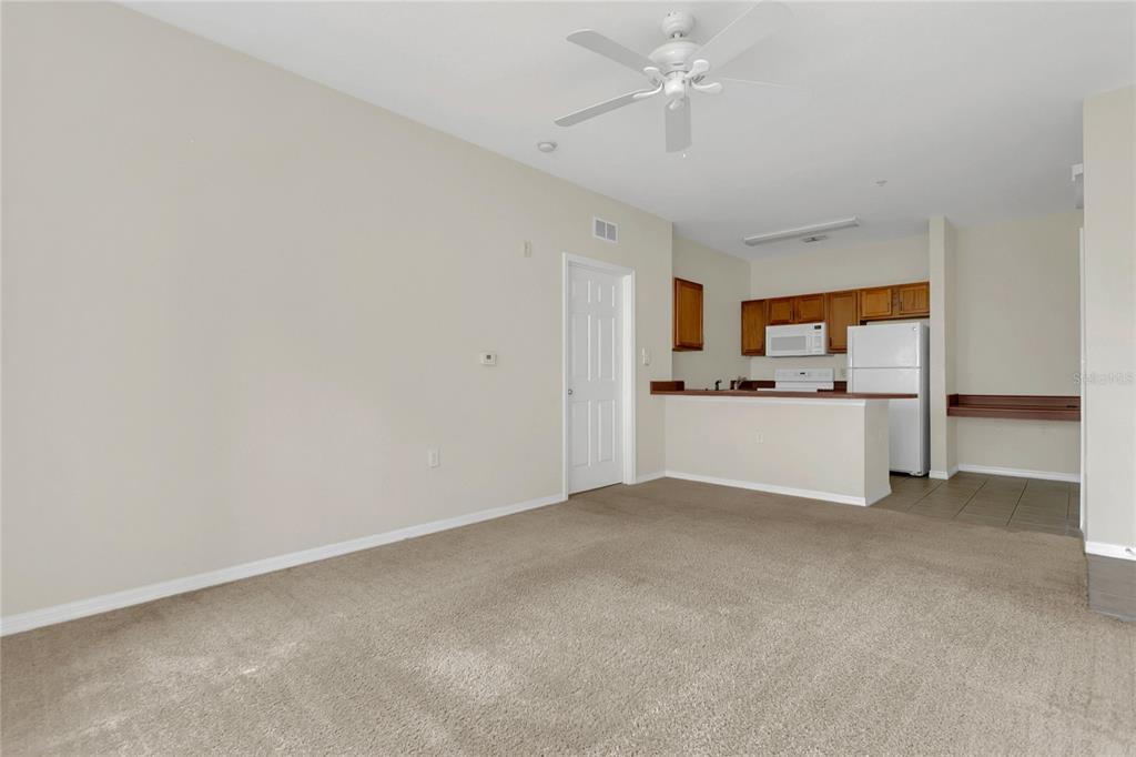 A carpeted living room opens to a kitchen with wooden cabinets and a breakfast bar — 8213 CLAIRE ANN DRIVE UNIT 108, ORLANDO, FL