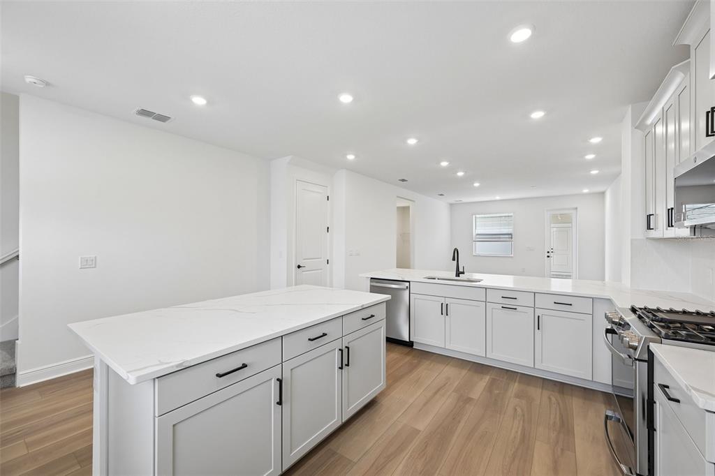 A modern kitchen features white cabinetry, a marble-topped island, and light wood-look flooring — 8229 SEAFLOWER PARKWAY, BRADENTON, FL