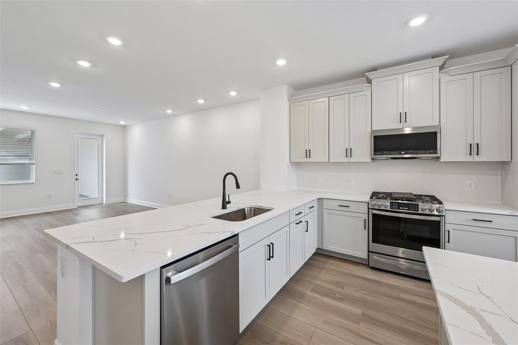 A modern kitchen features white cabinets, stainless steel appliances, and a marble-patterned quartz island — 8229 SEAFLOWER PARKWAY, BRADENTON, FL