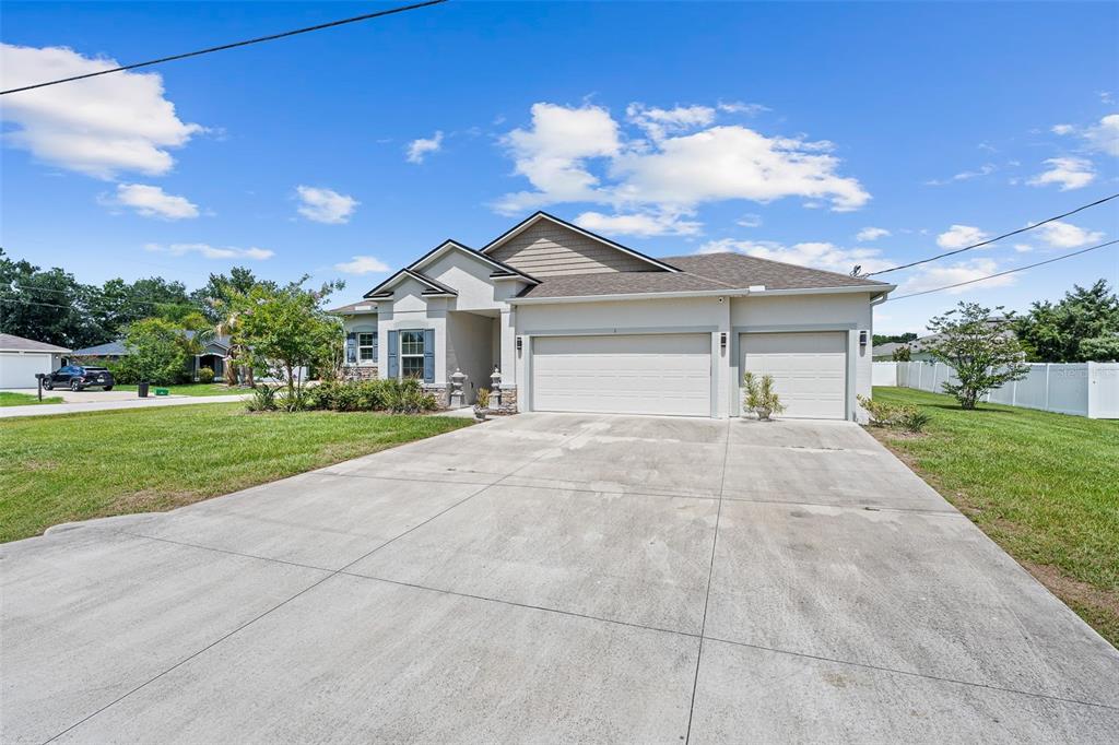 A single-story house features a three-car garage, a concrete driveway, and a light-colored exterior — 1 LYONS PLACE, PALM COAST, FL