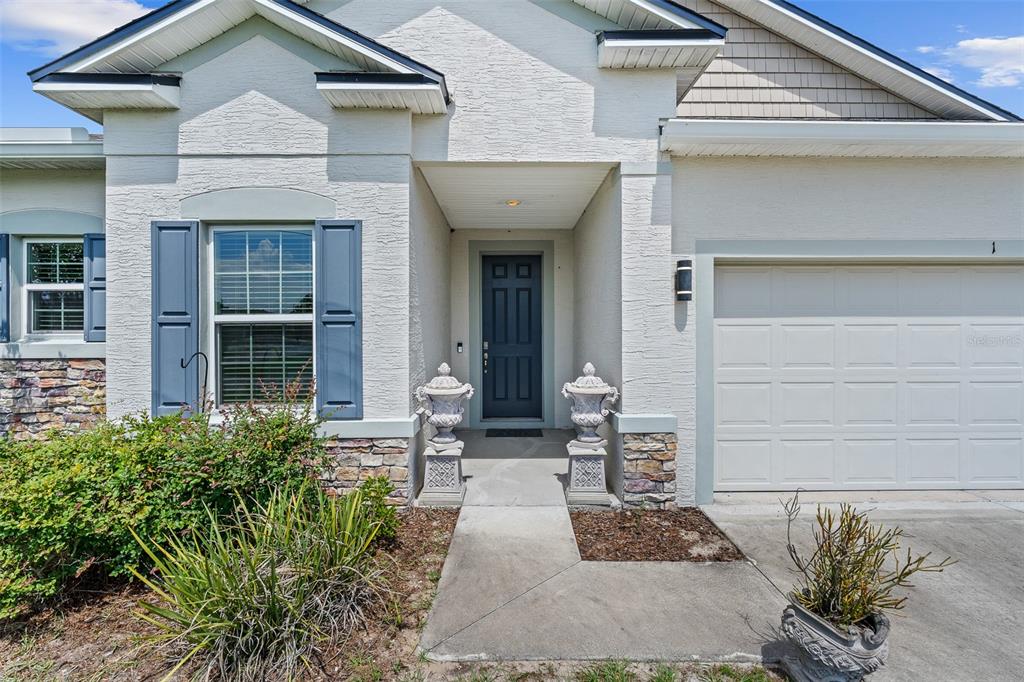 The exterior of a house features a front door, a garage, and stone veneer accents — 1 LYONS PLACE, PALM COAST, FL