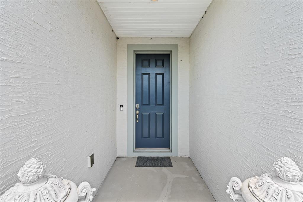 A dark blue front door is centered in a covered entryway with textured white walls — 1 LYONS PLACE, PALM COAST, FL
