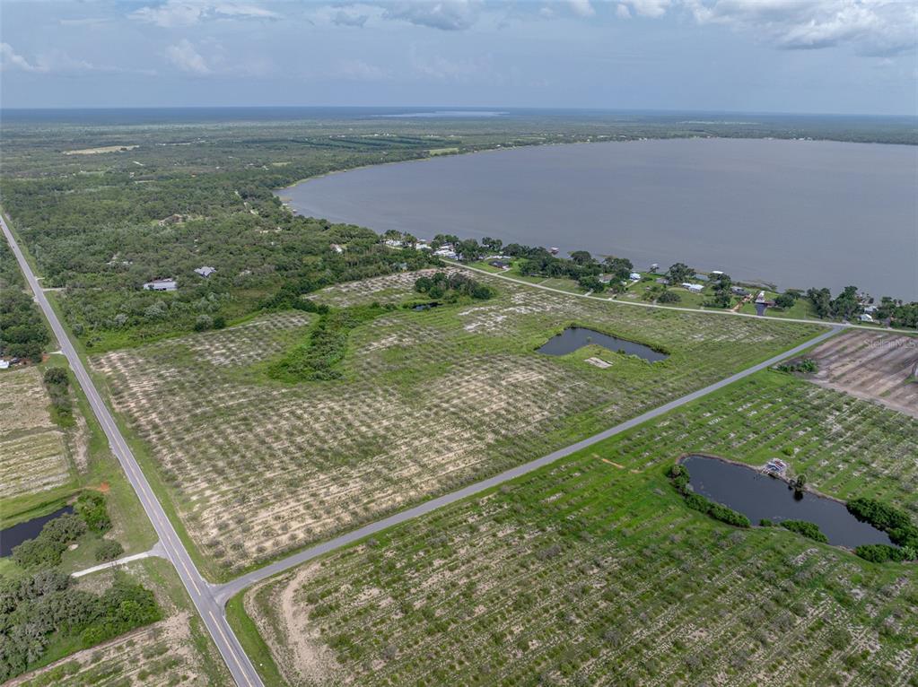 An aerial view shows a large, grassy lot with small trees near a lake — 0 LAKE REEDY BOULEVARD, FROSTPROOF, FL