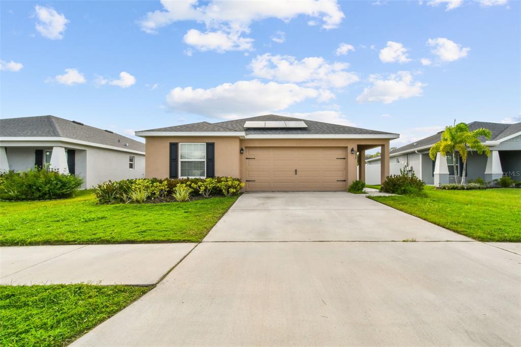 A tan single-story house with a two-car garage and a concrete driveway under a sky — 6977 ABBYWOOD LANE, ZEPHYRHILLS, FL