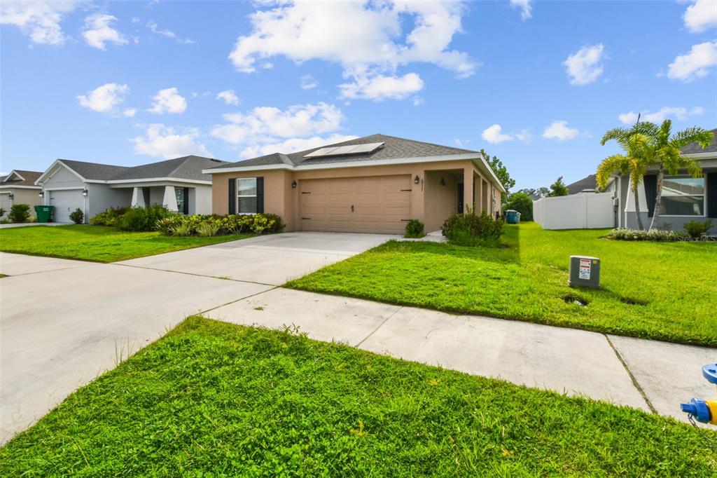 A tan single-story house with a two-car garage and solar panels on the roof — 6977 ABBYWOOD LANE, ZEPHYRHILLS, FL