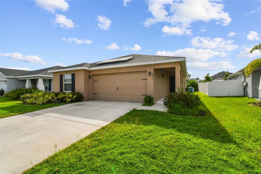 A tan single-story house with a two-car garage and a concrete driveway under a sky — 6977 ABBYWOOD LANE, ZEPHYRHILLS, FL