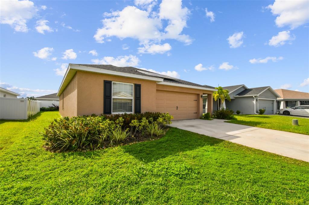 A tan single-story house with a two-car garage and a front yard lawn — 6977 ABBYWOOD LANE, ZEPHYRHILLS, FL