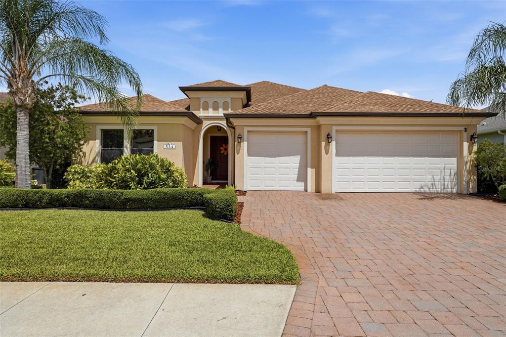 A single-story house with a tan stucco exterior, a paver driveway, and a three-car garage — 534 CHANTILLY TRAIL, BRADENTON, FL