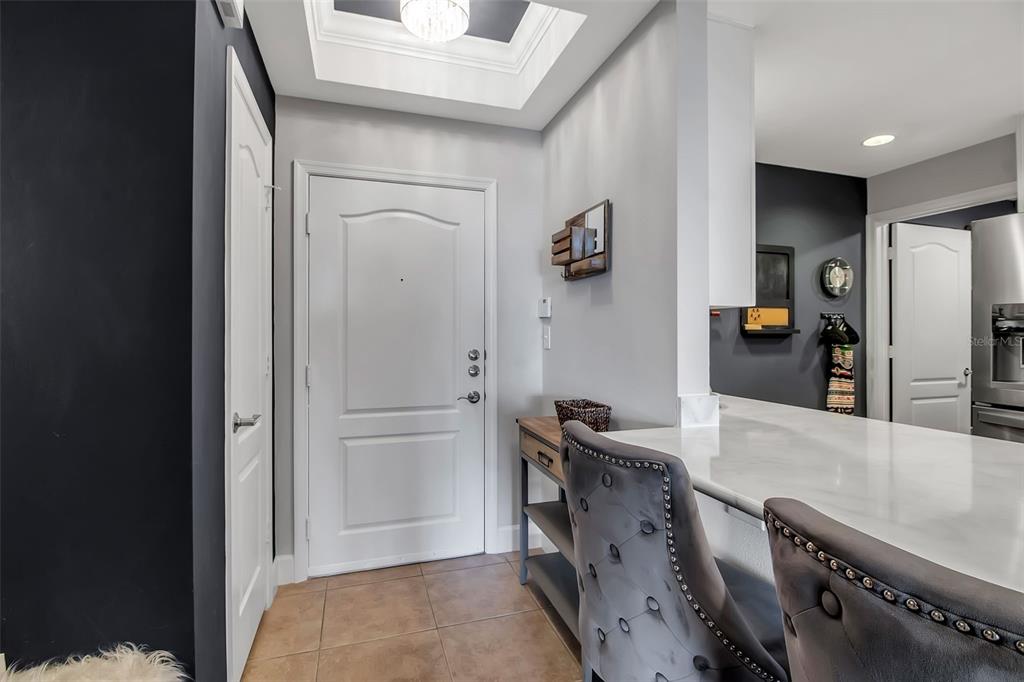 An entryway with a white door, tiled floor, and a breakfast bar with tufted chairs — 808 3RD AVENUE W UNIT 307, BRADENTON, FL