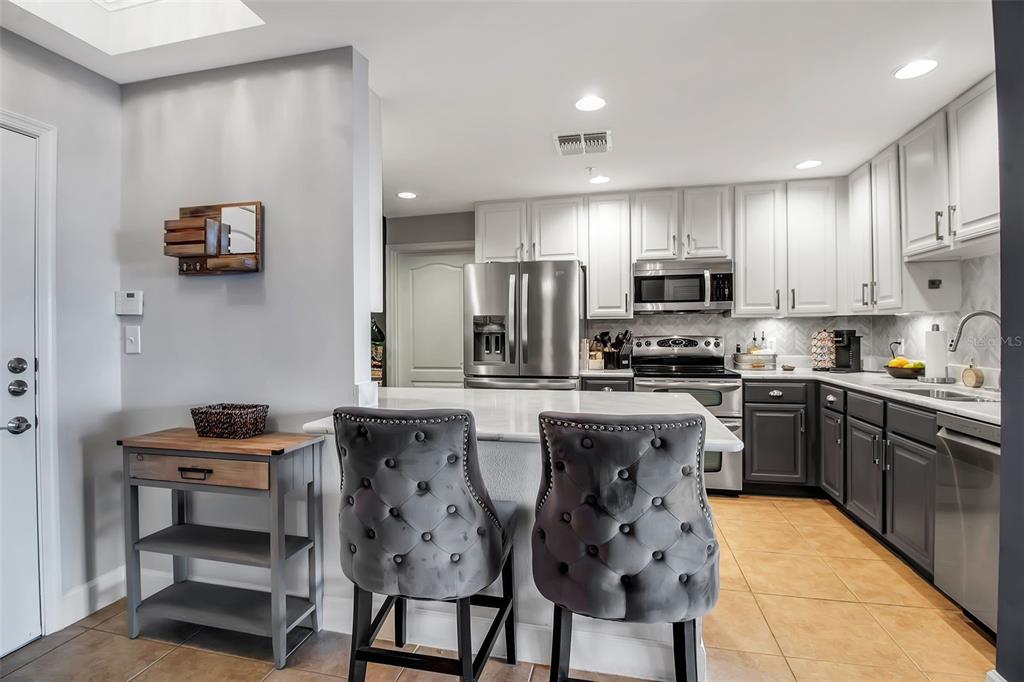 A kitchen features white upper cabinets, dark lower cabinets, a central island, and gray stools — 808 3RD AVENUE W UNIT 307, BRADENTON, FL