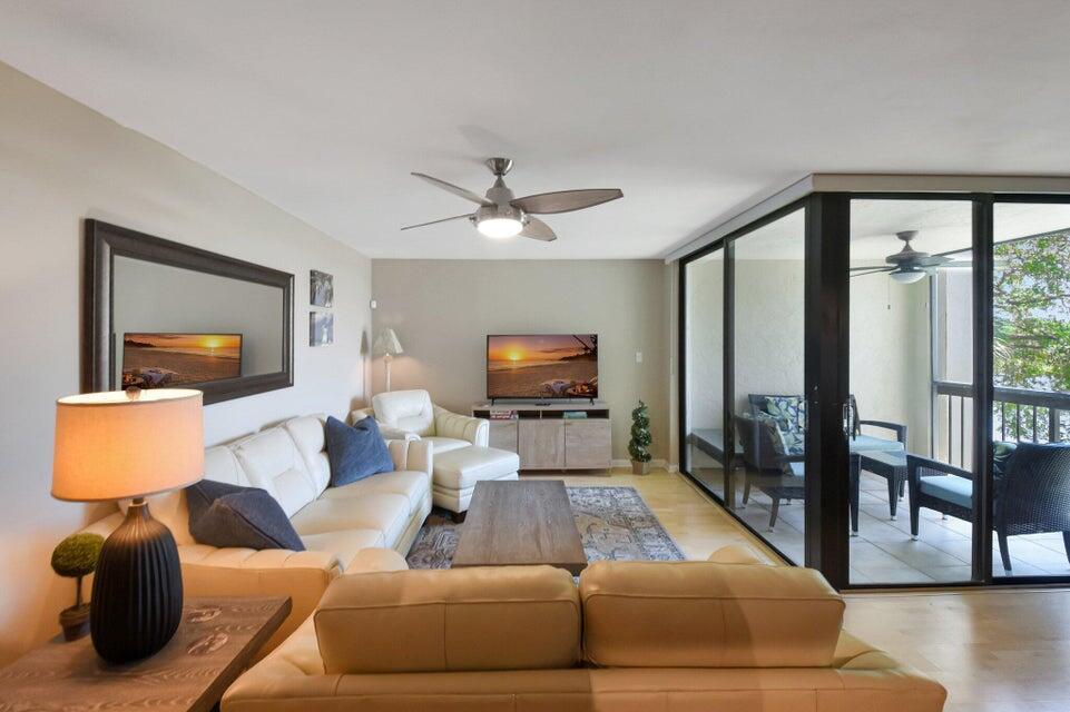 A living room features a beige sofa, a coffee table, a television, and a balcony — 950 Lavers Circle # F309, Delray Beach FL 33444, DELRAY BEACH, FL