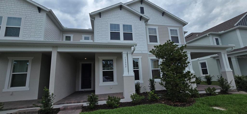 A two-story townhouse exterior features a covered front porch, light siding, and shingled accents — 13552 AUTUMN HARVEST AVENUE, WINTER GARDEN, FL