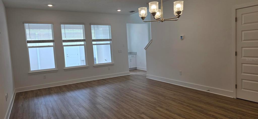 An empty room with wood-look flooring, three windows, a chandelier, and a white door — 13552 AUTUMN HARVEST AVENUE, WINTER GARDEN, FL