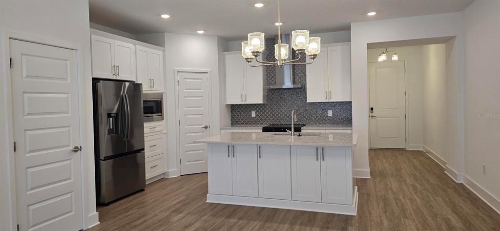 A modern kitchen features white cabinetry, stainless steel appliances, a center island, and patterned backsplash — 13552 AUTUMN HARVEST AVENUE, WINTER GARDEN, FL