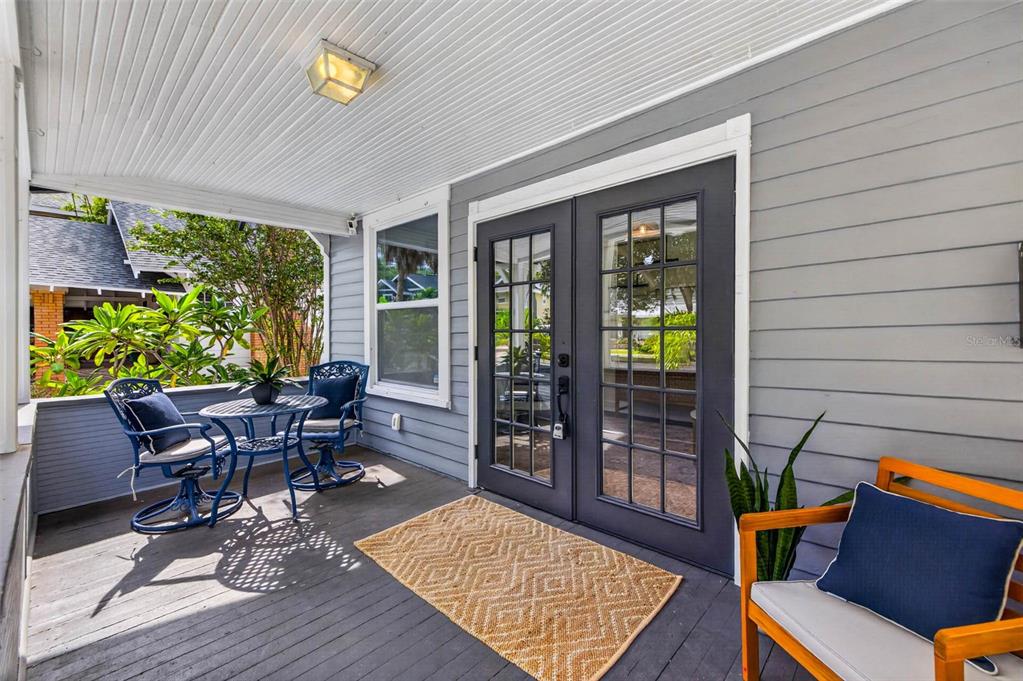 A covered porch features gray siding, double glass doors, and outdoor seating on a wooden deck — 629 6TH AVENUE N, ST PETERSBURG, FL
