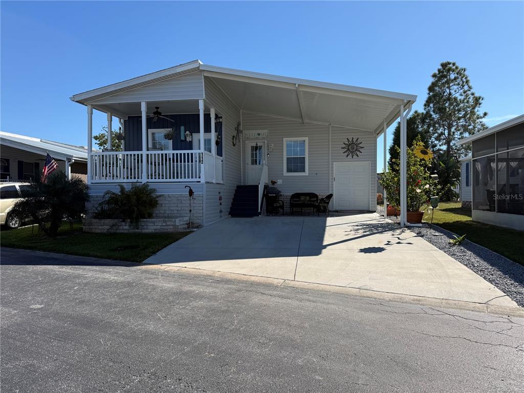A light-colored manufactured home features a front porch, a carport, and a concrete driveway — 9790 66TH STREET N UNIT 112, PINELLAS PARK, FL