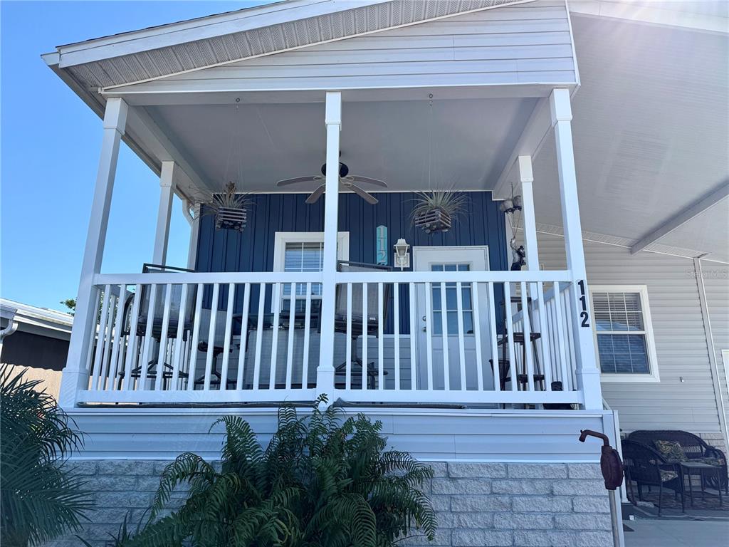 A raised front porch with white railings, a ceiling fan, and blue vertical siding — 9790 66TH STREET N UNIT 112, PINELLAS PARK, FL
