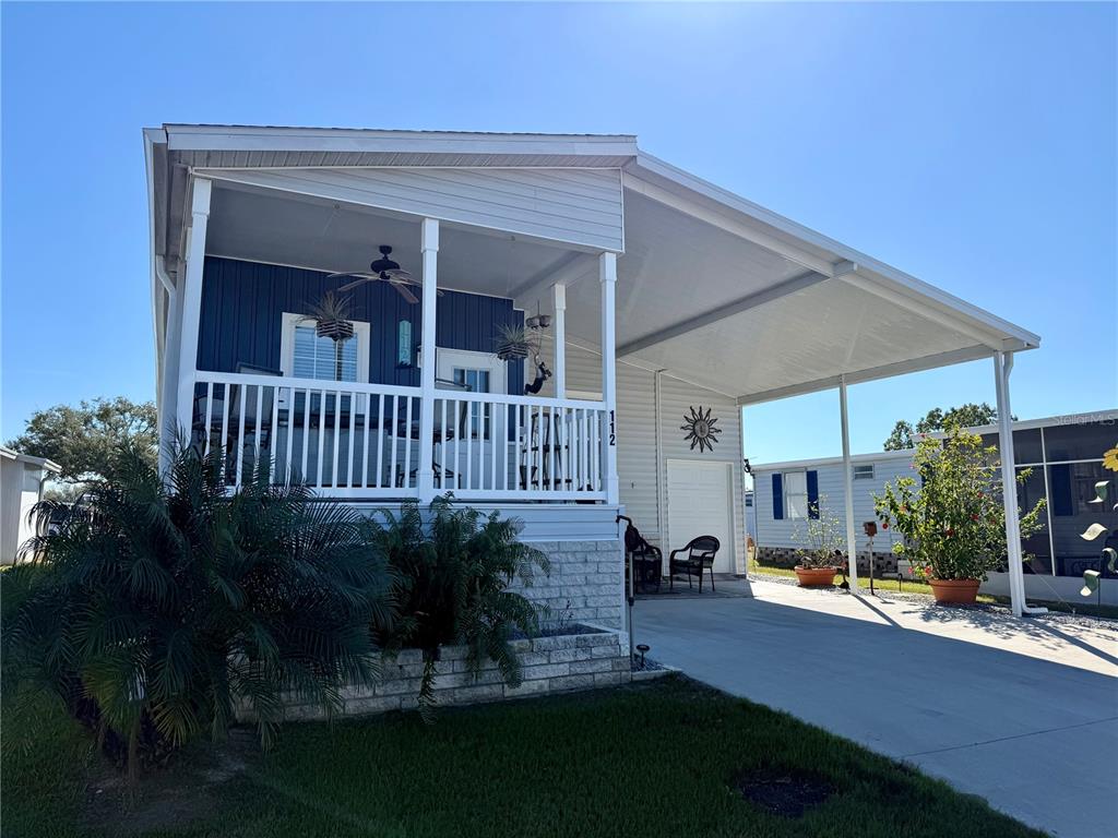 A mobile home with a covered porch, carport, and light-colored siding under a clear sky — 9790 66TH STREET N UNIT 112, PINELLAS PARK, FL