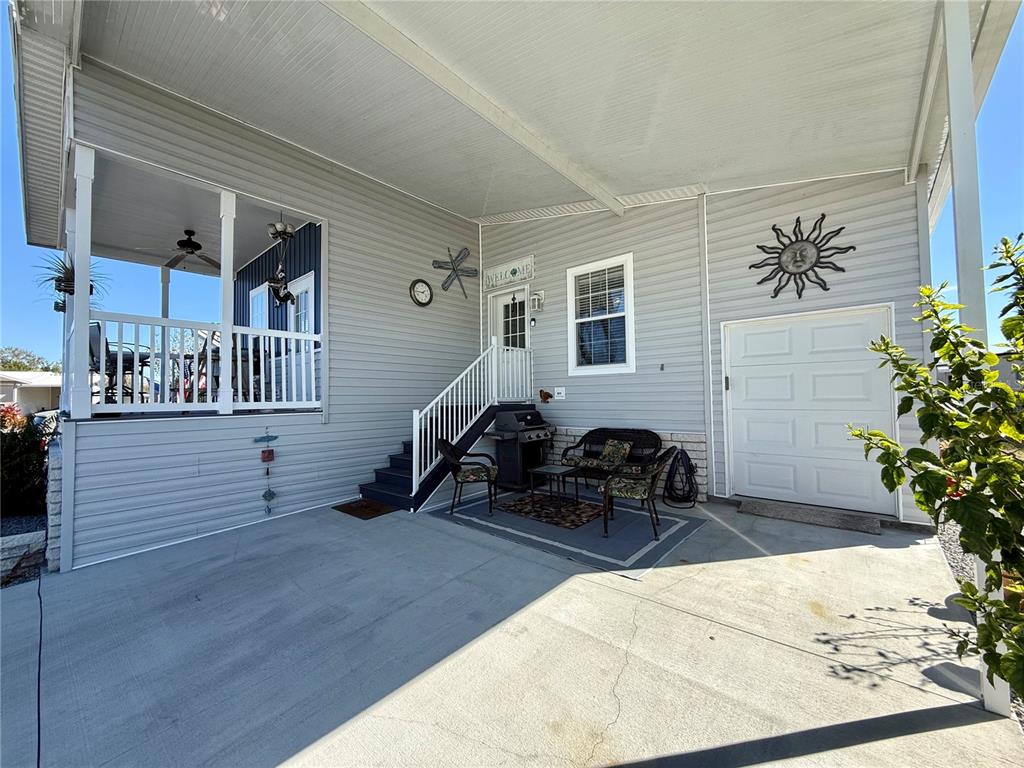 A concrete driveway leads to a covered patio with stairs, outdoor seating, and a garage door — 9790 66TH STREET N UNIT 112, PINELLAS PARK, FL